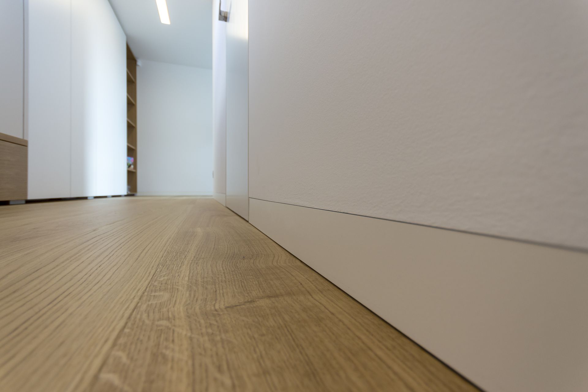 Dorsis LINUS recessed white baseboard installed flush with the wall above an oak floor